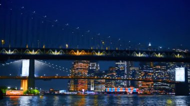 Arabalar gece güzel Manhattan Köprüsü 'nün yanından geçiyor. Arka planda New York 'un göz kamaştırıcı manzarası. Nehrin manzarası.
