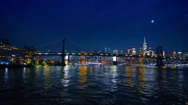İnanılmaz New York ışıkları Doğu Nehri 'nin karanlık sularını yansıtıyor. Manhattan Köprüsü 'nün alçak açılı görüntüsü ve geceleri nehirden şehrin ufuk çizgisi.