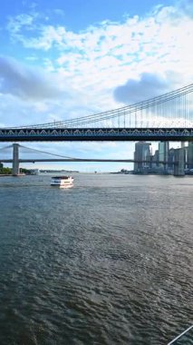 Doğu Nehri 'nin kıyısında Amerikan bayrağı taşıyan bir tekneyle seyahat ediyorlar. Manhattan Köprüsü ve Brooklyn Köprüsü. Dikey video.
