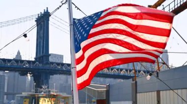 Rüzgarda dalgalanan Amerikan bayrağıyla gemi direği. Manhattan Köprüsü alçak açılı arkaplandan.