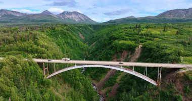Arabalar, Hurricane Gulch 'u geçen metal kemer köprüsünden hızla geçerler. Amerika, Alaska 'daki en yüksek köprülerden birine bakın..