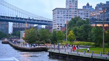 Bir sürü insan rıhtımın yanından bir parkla geçer. New York 'un yüksek binaları ve Manhattan Köprüsü.