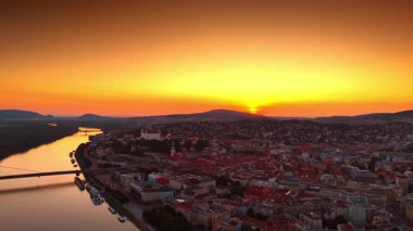 Batan güneş gökyüzünü, şehir manzarasını ve nehir yüzeyini turuncuya boyadı. Tuna ve Slovakya 'nın Bratislava kentinin üzerindeki insansız hava aracı görüntüleri..