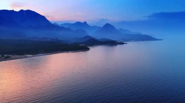 Dağların sislerle kaplı güzel siluetleri. Denizin ya da okyanusun kayalık sahillerinde alacakaranlık vakti. Hava görünümü.