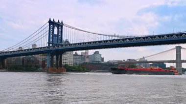 Manhattan Köprüsü 'nün altından Doğu Nehri' ne doğru yavaşça ilerleyen bir mavna. Arka planda New York silueti.