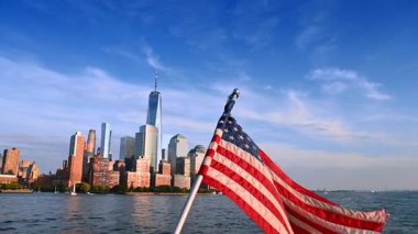 Parlak güneş ışığında Amerikan bayrağı sallıyor. Arka planda New York 'un silüeti. Nehrin manzarası.
