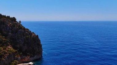 Açık gökyüzünün altında mavi okyanus manzarası. Geniş mavi okyanus ufka kadar uzanıyor. Parlak, berrak bir gökyüzünün altında engebeli kayalıklarla çevrili..