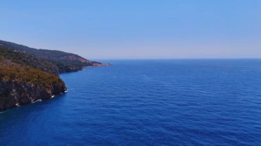 Açık mavi okyanus ve uçurumlar. Çarpıcı mavi okyanus ufka kadar uzanıyor, güneşli bir günde açık gökyüzünün altında engebeli kayalıklarla karşılaşmak..