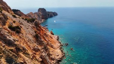 Kayalıklar ve berrak deniz suları. Kayalık kayalıklar berrak bir gökyüzünün altında canlı mavi sularla buluşur, doğayla dolu sakin bir kıyı manzarası sergilerler..