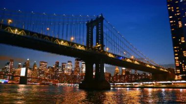 Manhattan Köprüsü 'nün ufuk çizgisi geceleyin. Manhattan Köprüsü gece aydınlanır, New York 'un canlı ufuk çizgisi su üzerinde sergilenir.