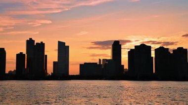 Nehirden gelen yüksek binaların ve çok katlı binaların siluetleri. New York 'un silüeti gün batımında turuncu gökyüzünün arka planında.