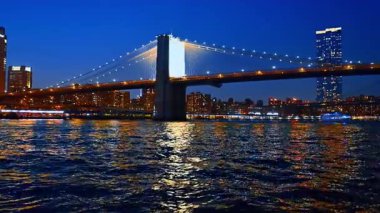 Nehir manzarasından çarpıcı Brooklyn Köprüsü 'nü izleyin. Doğu Nehri 'nde birden fazla sokak lambası yankılanıyor. New York 'ta gece tekne yolculuğu.