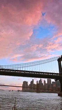 Manhattan Köprüsü 'nün üzerinde güzel, tüylü, pembe bulutlar. Doğu Nehri 'nin alçak açılı manzarası. Dikey video.