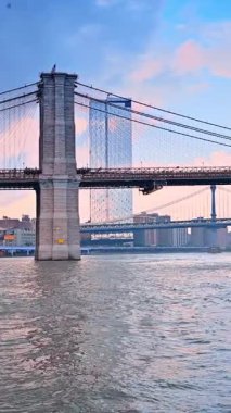 Ünlü Brooklyn Köprüsü Doğu Nehri 'ni geçiyor. Nehrin manzarası. Manhattan Köprüsü, arka planda. New York, ABD 'de tekne turu. Dikey video.