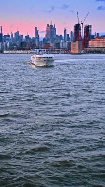 Su manzarasından beyaz nehir teknesi yaklaşıyor. Günbatımında New York 'un yoğun modern silueti. Dikey video.