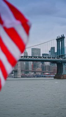 Manhattan Köprüsü 'nün yanındaki nehirde tekne yolculuğu. Amerikan bayrağı kameraya dalgalanıyor. New York, ABD 'de gri bir gün. Dikey video.
