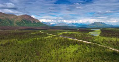 Ormanlık vadi boyunca giden trene yetişmek. Alaska 'nın göz kamaştırıcı doğa manzarası üzerinde İHA görüntüleri. Resimli dağlarla çevrili..
