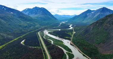 Dağın eteğindeki muhteşem vadiyi geçen bir nehir ve otoyol. Alaska 'nın muhteşem doğa manzarası üzerinde insansız hava aracı görüntüleri.
