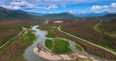 Alaska 'nın geniş vadisindeki dallanan nehrin üzerindeki görüntüler. Arabalar otobanın yanından geçerek arka plandaki dağlara doğru gidiyor..