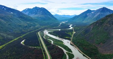 Dağın eteğindeki muhteşem vadiyi geçen bir nehir ve otoyol. Alaska 'nın muhteşem doğa manzarası üzerinde insansız hava aracı görüntüleri.