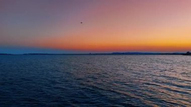 Koyu mavi deniz manzarası üzerinde uçmak. Şehir ışıkları ve dağ siluetleri gün batımında pembe gökyüzünün arkaplanında.