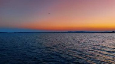 Koyu mavi deniz manzarası üzerinde uçmak. Şehir ışıkları ve dağ siluetleri gün batımında pembe gökyüzünün arkaplanında.