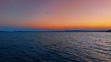 Koyu mavi deniz manzarası üzerinde uçmak. Şehir ışıkları ve dağ siluetleri gün batımında pembe gökyüzünün arkaplanında.