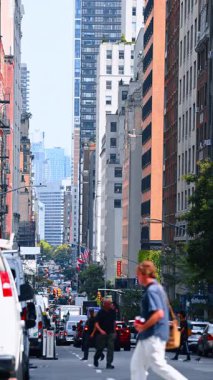 New York 'un modern caddesinde yoğun bir trafik var. Bir sürü insan karşıdan karşıya geçiyor. Dikey video.