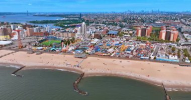 Kumsalda uçarken birkaç kişi dinleniyor. Güneşli bir günde Coney Adası, Brooklyn, New York 'taki lunaparkın görüntüsü.