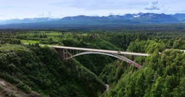 Alaska güzeliyle bağlantı kurmak. Alaska 'da bereketli bir kanyon boyunca uzanan, görkemli dağlar ve yeşilliklerle çevrili çarpıcı bir köprü manzarası..