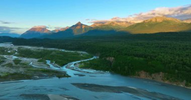 Alaska nehirleri ve dağları. Güneşin batışı sırasında Alaska 'da berrak bir gökyüzünün altında yükselen dağlarla görkemli nehirler yemyeşil arazide akar..