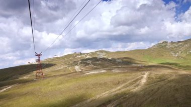 Kablolu yayla dağ manzarası üzerinden geçiyor. Gün boyunca bulutlu bir gökyüzünün altında yemyeşil tepeler üzerinde süzülen bir teleferik..
