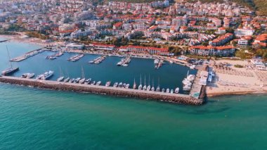 Turkuaz su dalgaları taşlı barajı vurdu. Tekneler ve yatlar rıhtımda duruyor. Bulgaristan 'ın güneşli Sveti Vlas kentinde çok sayıda otel.