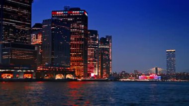 Şehrin yüksek gökdelenlerinin ışıkları nehir manzarasını yansıtıyor. Alacakaranlıkta Doğu Nehri 'nde tekne gezintisi. Arkaplanda aydınlatma olan Brooklyn Köprüsü.