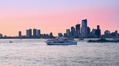 Günbatımında çok çeşitli yelkenliler su yüzeyinde duruyor. New York 'un silüeti Pembe gökyüzünün arka planında.
