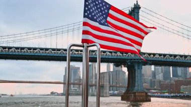 Teknenin önünde dalgalanan Amerika bayrağı. Ünlü Manhattan Köprüsü ve New York silueti.