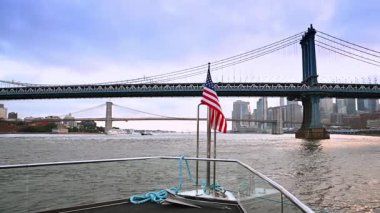 Teknenin ön kısmından Amerikan bayrağıyla çekilmiş görüntüler. Manhattan Köprüsü ve New York ufuk çizgisinde görünüm.