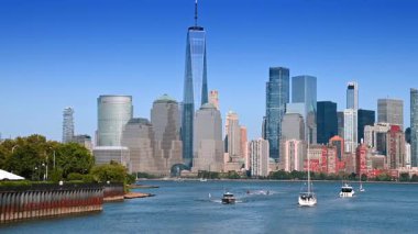 Güneşli bir günde Hudson Nehri 'nde çeşitli su araçları. İnsanlar nehir kenarında yürür. Jersey 'in karşısındaki Manhattan' a bak..