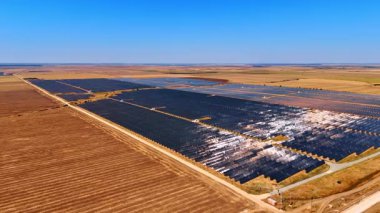 Güneş, kırsal bölgeye kurulmuş güneş panellerini kamaştırıyor. Enerji üretim alanlarını çevreleyen geniş çıplak alanlar. Hava görünümü.