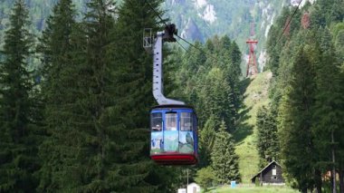 Ormandaki dağın üzerinden geçen kablo araba. Bir teleferik, dağlık bir bölgede, sık ağaçların üzerinde seyahat eder. Güzel manzaralar ve açık gökyüzü sergiler..
