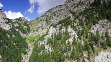 Görkemli yeşil dağ manzarası. Parlak mavi gökyüzünün altındaki yemyeşil bir vadinin tepesindeki kayalık kulede dağınık bulutlar var..
