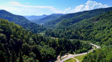 Dolambaçlı yolu olan sakin dağ vadisi. Bereketli yeşil dağlar, açık mavi gökyüzünün altında dolambaçlı bir yolu olan, dolambaçlı bir vadiyi çevreleyen ve doğanın güzelliğini gözler önüne seren..