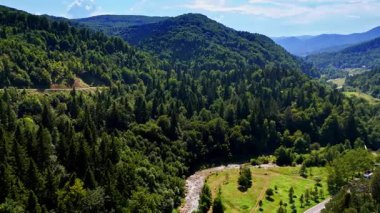 Bereketli dağların ve nehrin manzarası. Bereketli yeşil dağlar, dolambaçlı bir nehrin etrafını sarar. Parlak mavi bir gökyüzünün altında, huzurlu bir doğal ortamda..