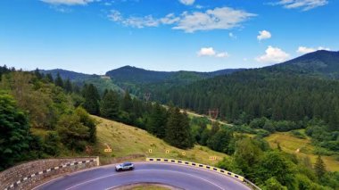Yeşil dağlarda virajlı bir yol. Açık mavi gökyüzünün altında kıvrımlı bir yol kıvrılarak doğanın güzelliğini gözler önüne seriyor..