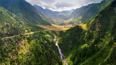Vadinin ötesindeki muhteşem dağlarda akan bir nehirin görüntüsü. Arabalı bir otoyol kayalıklardaki vadiyi geçer. Romanya 'nın doğasıyla ilgili hava görüşü.