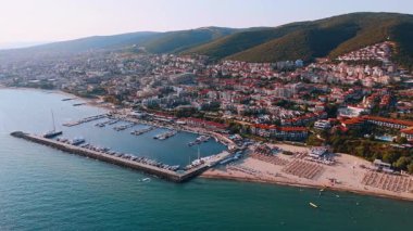 Muhteşem marina sahili manzarası. Berrak gökyüzünün altında canlı bir marina ve kumlu sahil manzarası, tepeler ve renkli binalarla çevrili..