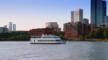 Nehir kıyısında tekne gezintisi. Pürüzsüz bir tekne, açık bir günde, canlı şehir binalarıyla çevrili nehirde sorunsuzca seyahat eder..