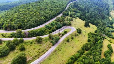 Yemyeşil tepelerden geçen dolambaçlı bir yol. Manzaralı bir yol, ağaçlarla çevrili yoğun yeşil tepeler ve gündüz vakti doğal güzellikler arasında kıvrılır..