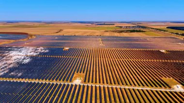 Açık gökyüzünün altında büyük bir güneş alanı. Güneş panelleriyle dolu geniş bir alanda parlayan güneş ışığı kırsal alanda yenilenebilir enerji potansiyeli gösteriyor..