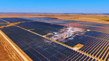 Büyük kırsal güneş çiftliği. Geniş bir güneş çiftliği berrak bir gökyüzü altında güneş ışığını kullanan sıra sıra paneller barındırır..